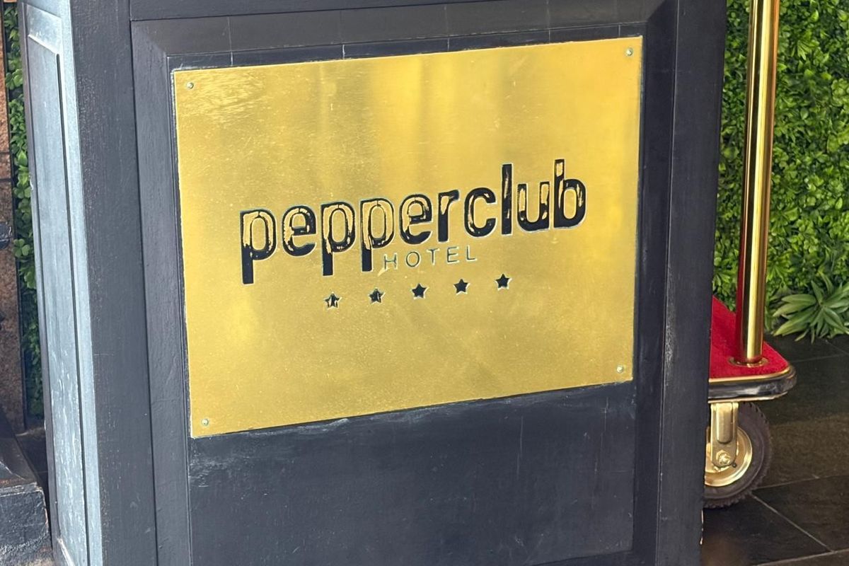 Close-up view of the Pepperclub Hotel signage featuring a gold-toned plaque mounted on a dark structural pillar at the property entrance.
