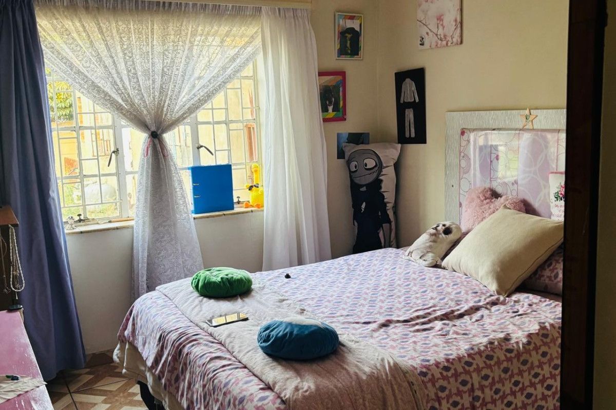 A cozy bedroom featuring tiled flooring, a large window with natural light, and a built-in headboard area.