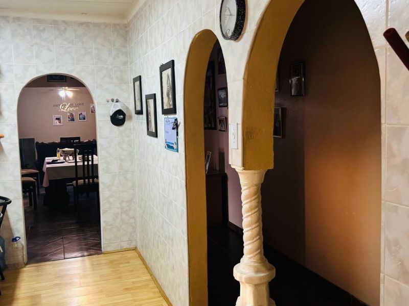A hallway featuring distinctive arched doorways with decorative pillars, connecting to adjacent living spaces with tiled walls and mixed flooring.