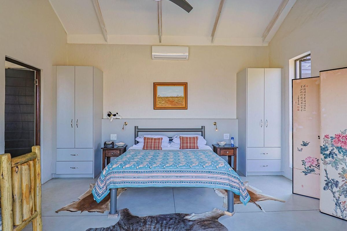 A spacious bedroom featuring vaulted ceilings with exposed beams, built-in cupboards, and a wall-mounted air conditioning unit.