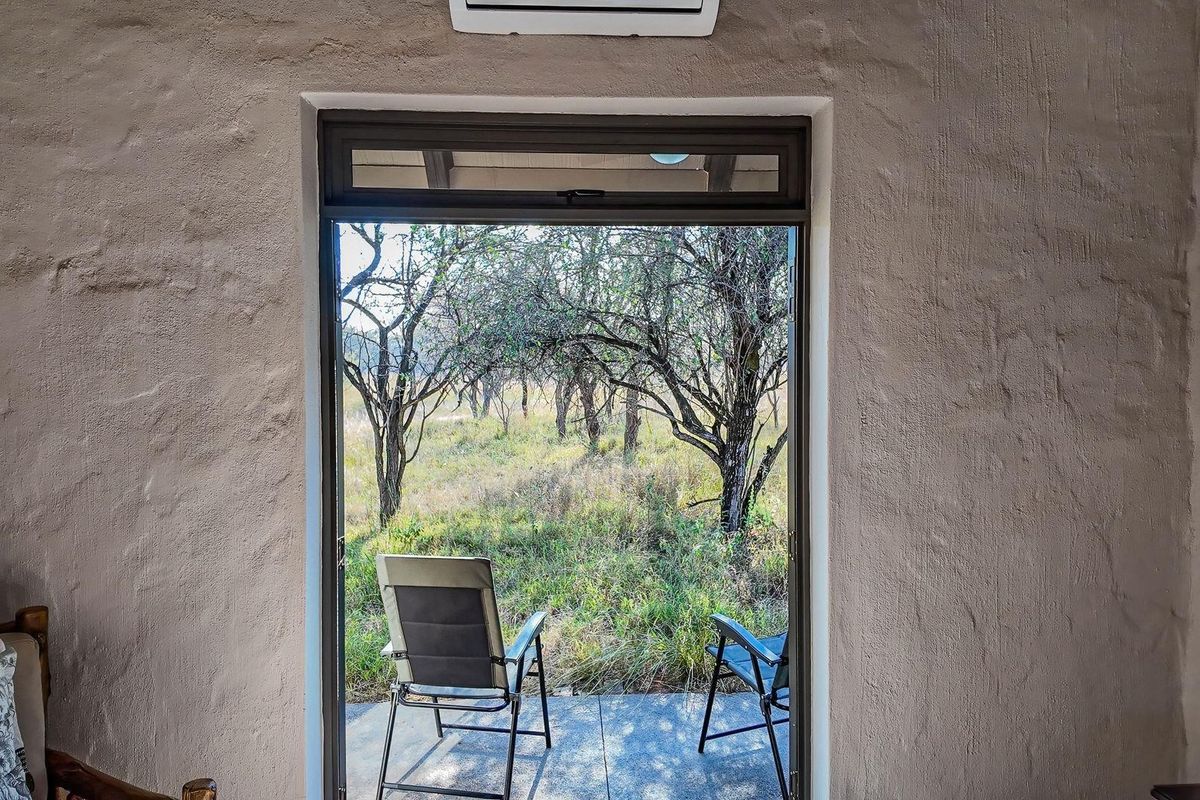 A view from an interior space looking out through a glass door onto a natural farm landscape with mature trees.