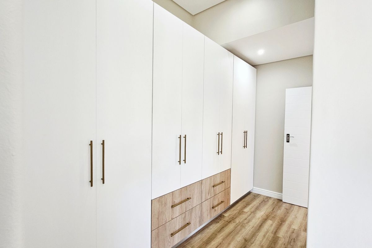 A modern bedroom featuring extensive floor-to-ceiling built-in cabinetry with a mix of white and wood-grain finishes, complemented by sleek brass hardware.