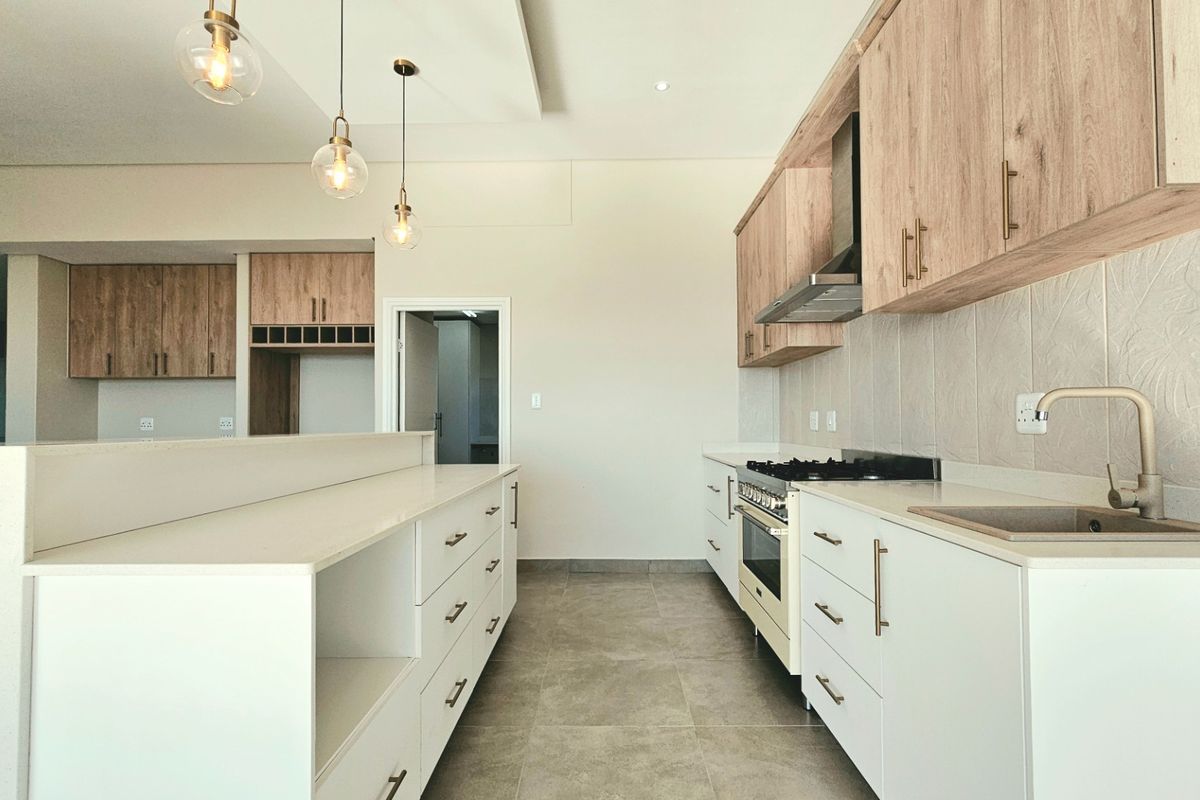 Modern kitchen featuring light wood cabinetry, white stone countertops, a gas stove, and a central island with integrated storage.