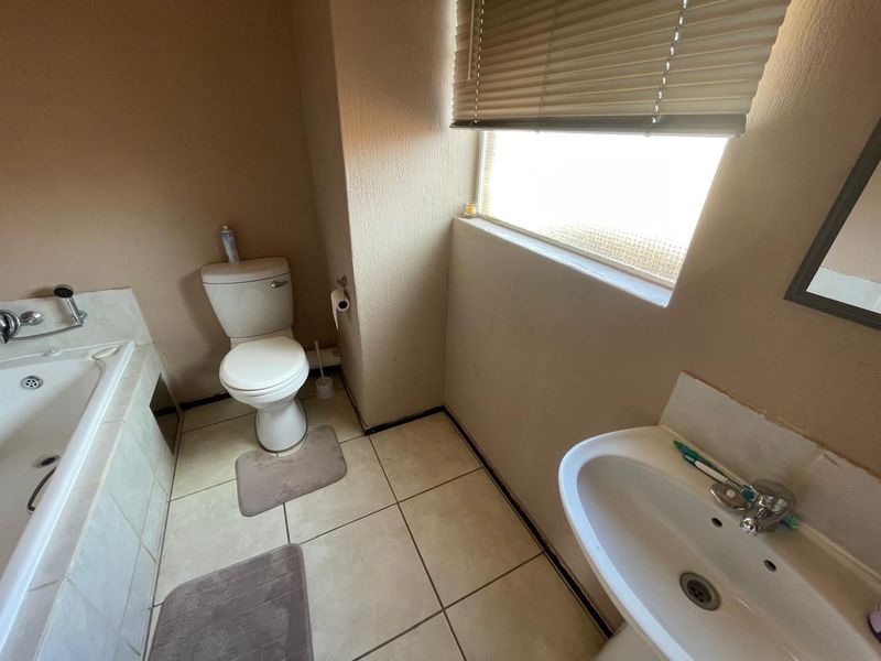 A functional bathroom featuring a built-in bathtub, pedestal sink, and toilet, with tiled flooring and a window providing natural light.
