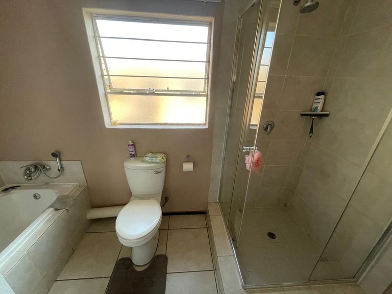 A functional bathroom featuring a built-in bathtub, a separate glass-enclosed shower, and a standard toilet with tiled flooring and a window.