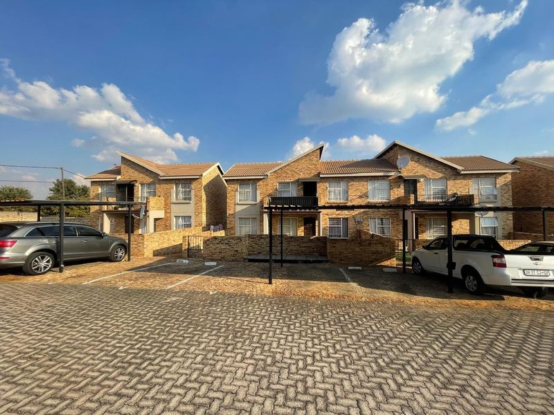 Exterior view of a multi-unit apartment complex featuring face-brick facades, tiled roofs, and dedicated covered parking bays for residents.