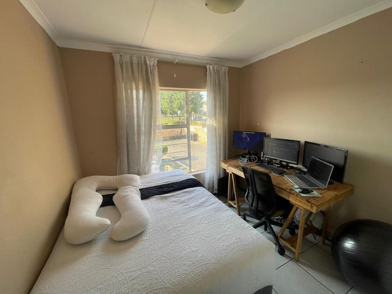 A functional bedroom featuring tiled flooring, a large window with natural light, and neutral wall tones, suitable for use as a sleeping area or office.