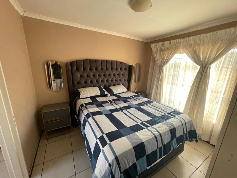 A bedroom featuring tiled flooring, neutral wall tones, and a large window with curtain tracks, providing a functional and comfortable sleeping space.