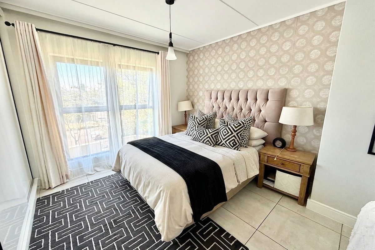 A well-maintained bedroom featuring tiled flooring, a decorative patterned feature wall, and a large window allowing for ample natural light.