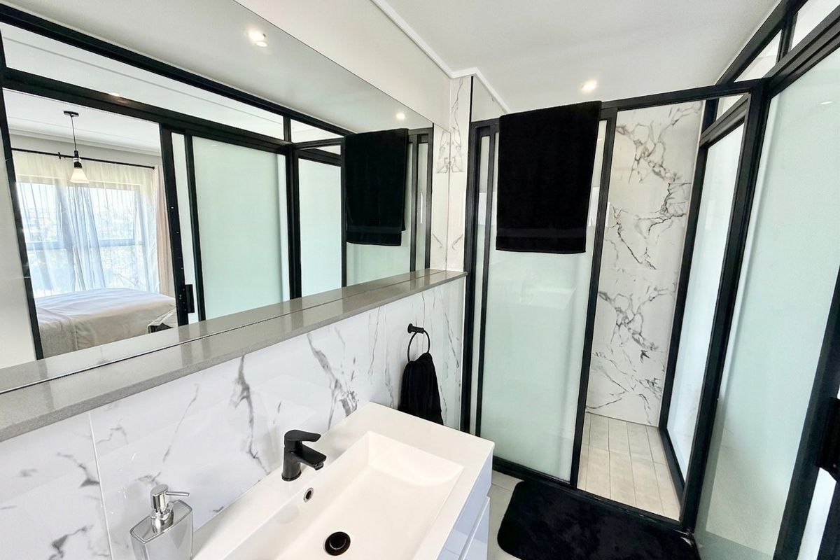 Modern bathroom featuring a sleek vanity with basin, large wall mirror, and a walk-in shower with marble-look tiling and black frame accents.