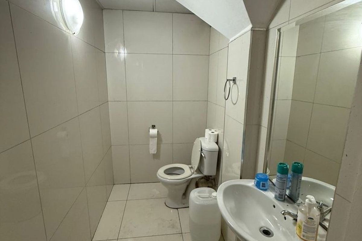 A compact bathroom featuring tiled walls and floors, a pedestal washbasin, and a standard toilet. The space requires minor maintenance and cosmetic updates.