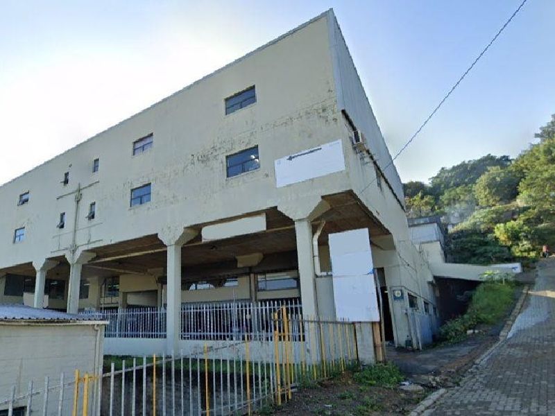 Industrial building exterior featuring concrete structural pillars, metal security fencing, and a paved driveway approach with visible signs of weathering.