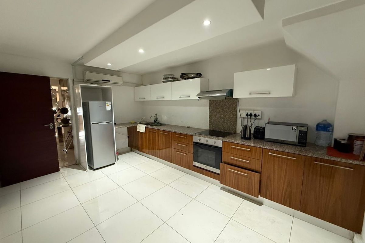 Modern kitchen featuring wood-finish cabinetry, granite countertops, integrated oven and hob, recessed lighting, and tiled flooring in a clean, functional layout.
