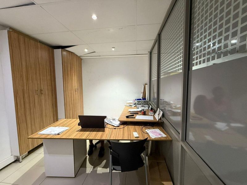 A functional office space featuring built-in wood-grain cabinetry, a glass partition wall, and tiled flooring with recessed ceiling lighting.