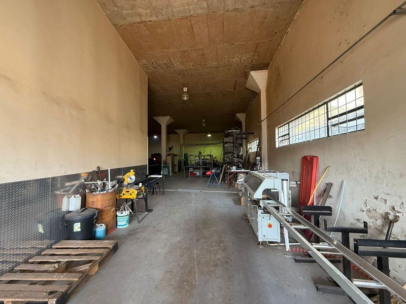 Spacious industrial utility area featuring concrete flooring, high ceilings, and diamond plate wall accents, suitable for workshop or storage operations.