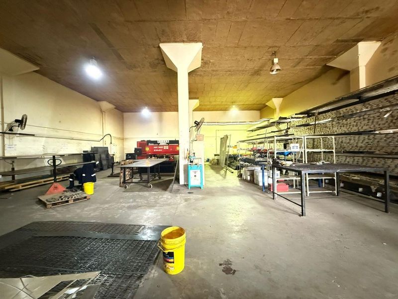 Spacious industrial utility area featuring concrete flooring, exposed ceiling, structural columns, and extensive built-in metal racking for storage and manufacturing operations.