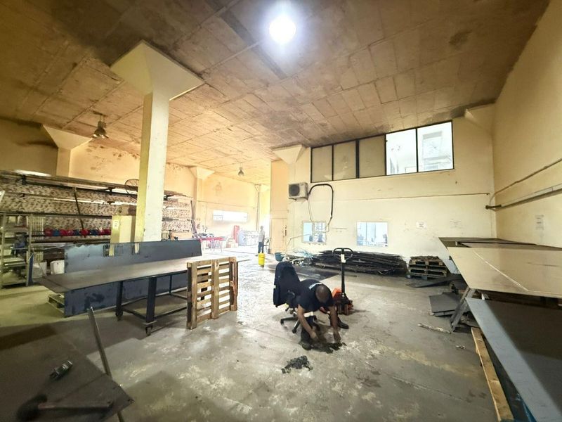 Spacious industrial utility area featuring high concrete ceilings, concrete flooring, and structural support columns, suitable for manufacturing or storage operations.