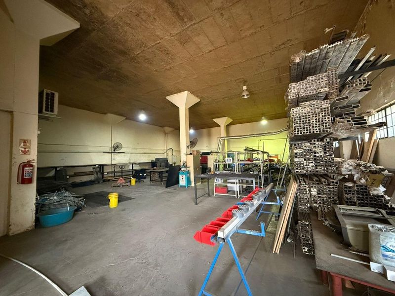 Industrial utility space featuring high concrete ceilings, structural columns, and concrete flooring, currently utilized for storage and workshop operations.