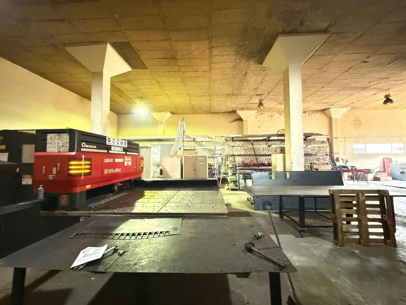 Industrial workshop space featuring high concrete ceilings, structural columns, and concrete flooring, currently utilized for heavy machinery and manufacturing operations.
