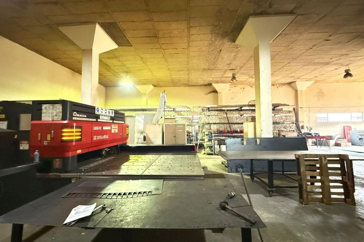 Industrial workshop space featuring high concrete ceilings, structural columns, and concrete flooring, currently utilized for heavy machinery and manufacturing operations.
