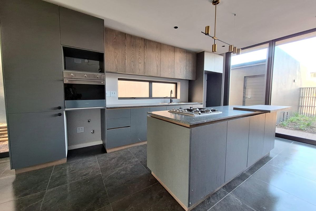 Modern open-plan kitchen featuring a central island with a built-in gas hob, sleek cabinetry, and large format floor tiles.