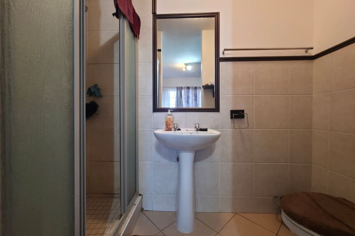 A functional bathroom featuring a pedestal basin, shower enclosure, and neutral wall tiling, offering a clean and practical layout.