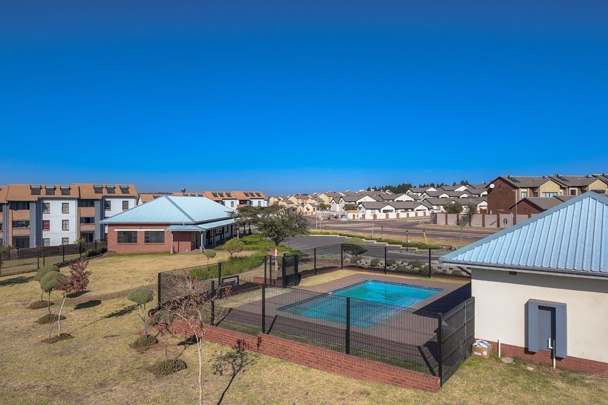 Aerial view of a residential complex featuring a communal swimming pool with secure fencing and landscaped grounds.