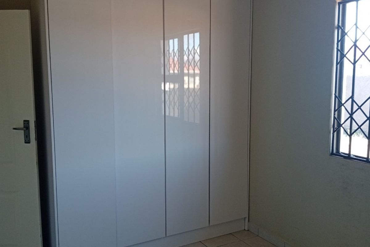 A clean bedroom featuring built-in white cabinetry, tiled flooring, and a window fitted with security bars.