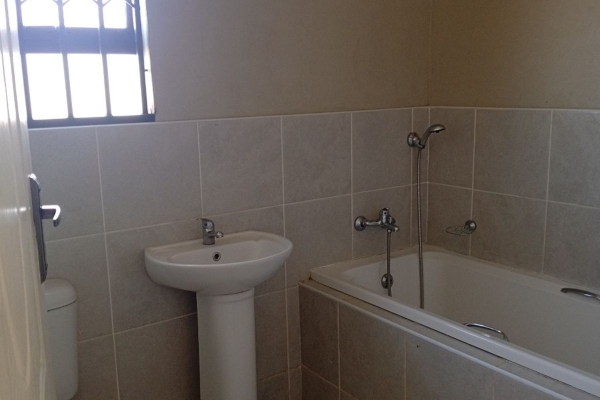 A functional bathroom featuring a pedestal basin, a bathtub with a handheld shower attachment, and a window with security bars.