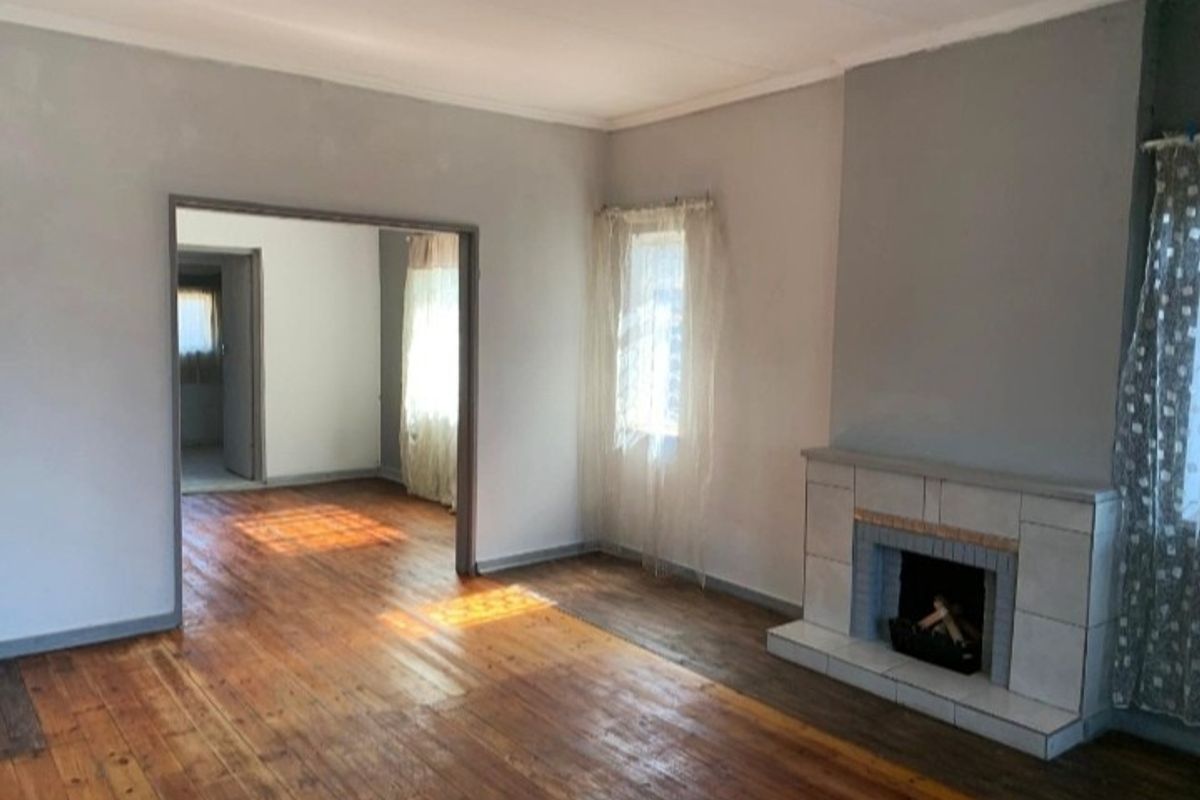 Spacious living room featuring original hardwood flooring and a classic tiled fireplace, offering a bright and open layout.