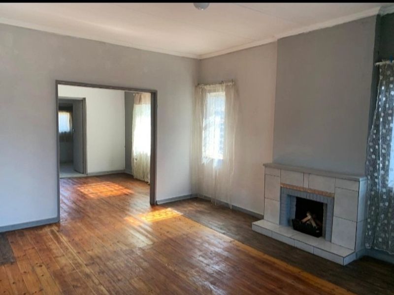 Spacious living room featuring original hardwood flooring and a classic tiled fireplace, offering a bright and open layout.