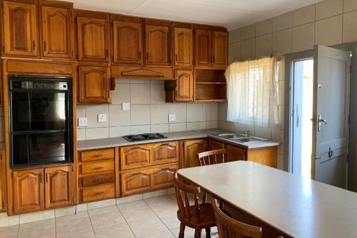 A functional kitchen featuring traditional wooden cabinetry, built-in oven, gas hob, and tiled finishes, offering a classic layout with direct outdoor access.
