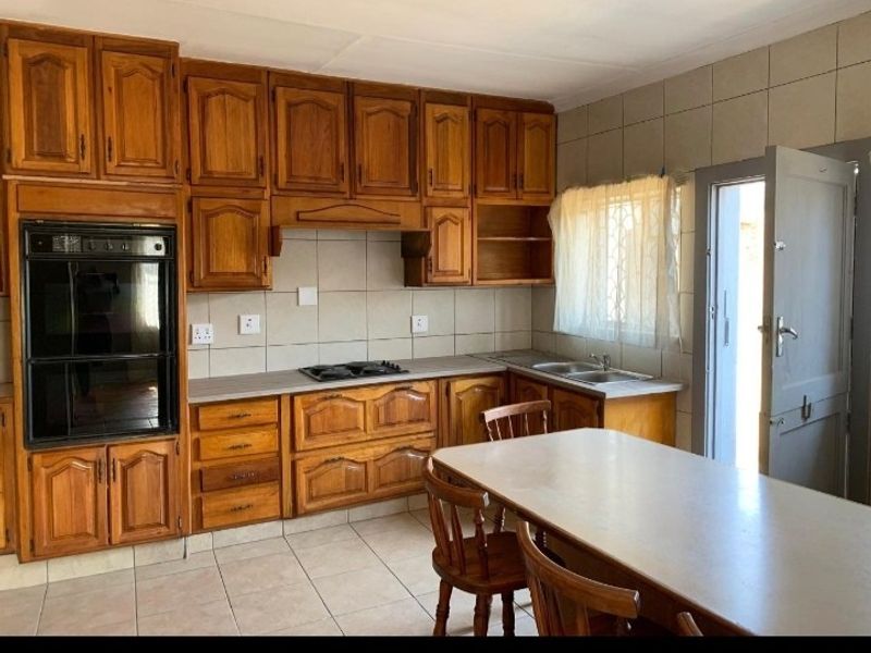 A functional kitchen featuring traditional wooden cabinetry, built-in oven, gas hob, and tiled finishes, offering a classic layout with direct outdoor access.