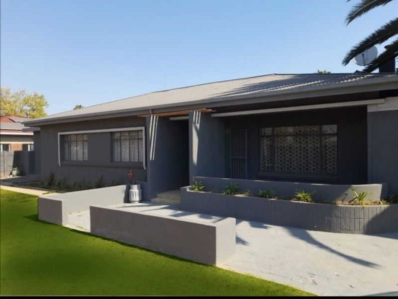 Front elevation of a single-story house featuring a grey painted facade, concrete planter boxes, and a paved entrance area.