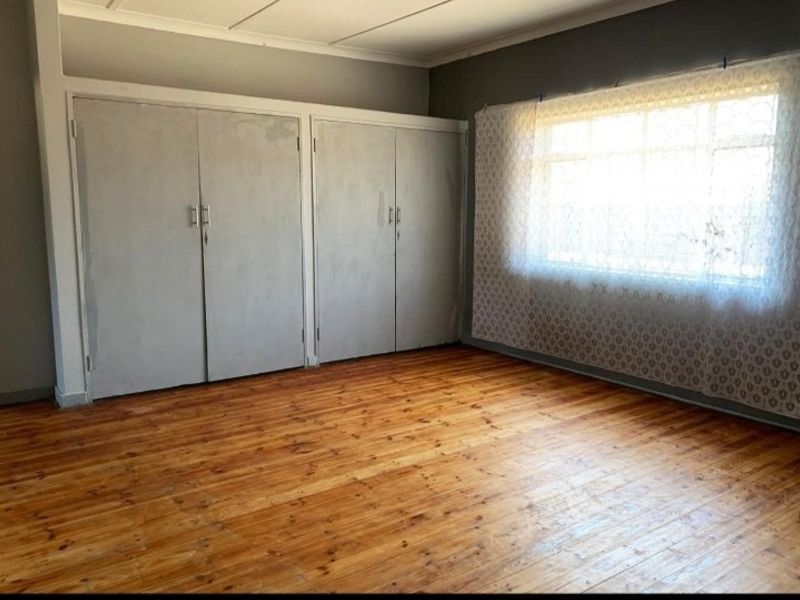 A spacious bedroom featuring polished timber flooring and extensive built-in cupboard storage, offering a clean and functional living space.