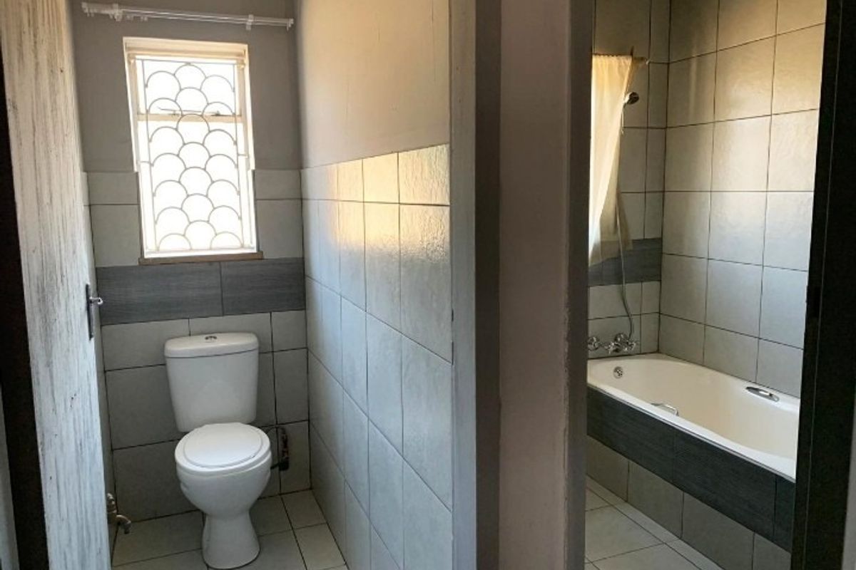 A functional bathroom featuring a toilet and a bathtub with shower mixer, finished with neutral wall and floor tiling.