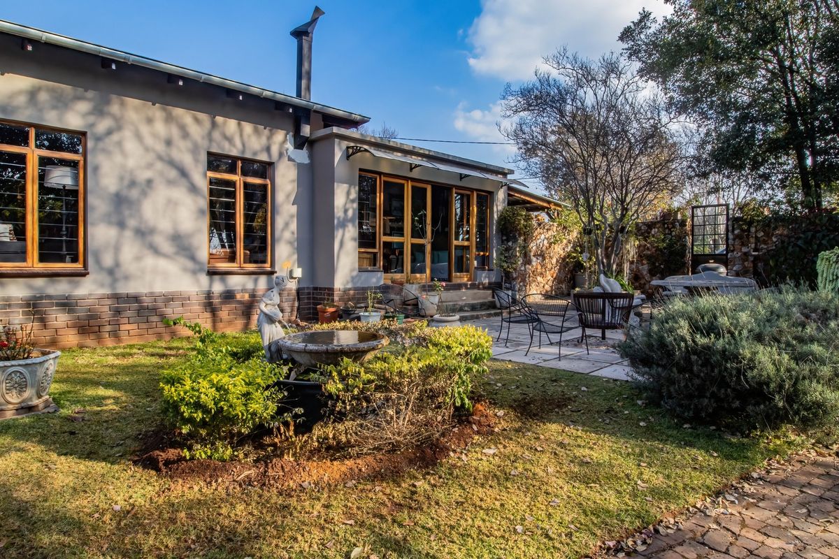 A rear view of the house featuring a paved patio area, landscaped garden, and wooden-framed windows and doors.