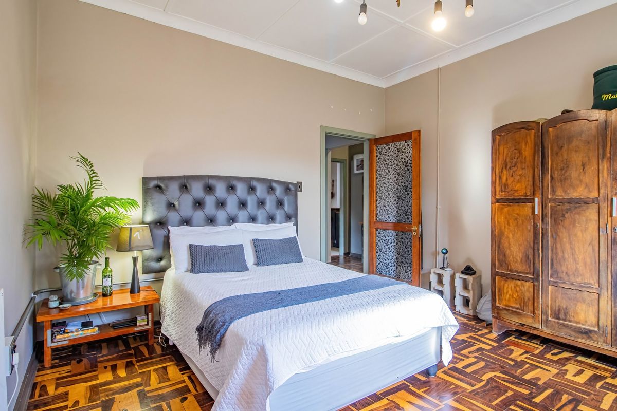 A bedroom featuring parquet flooring, a tufted headboard, and a wooden door leading to an adjacent hallway.