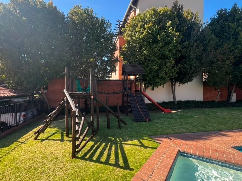 Outdoor communal area featuring a swimming pool with brick coping, manicured lawn, and perimeter fencing within a residential apartment complex.