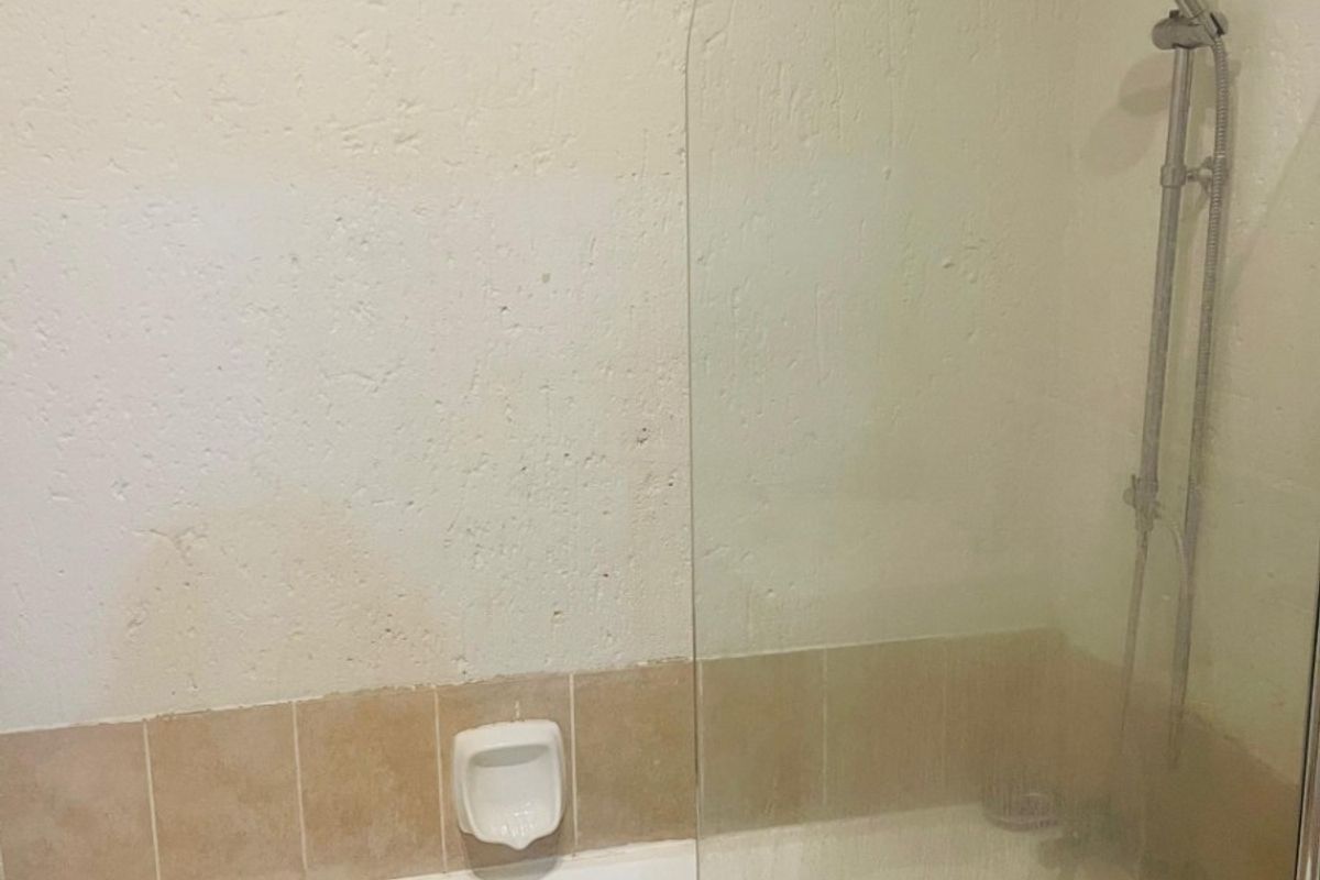 A bathroom featuring a bathtub with a glass shower screen, overhead rainfall shower head, and handheld shower attachment.