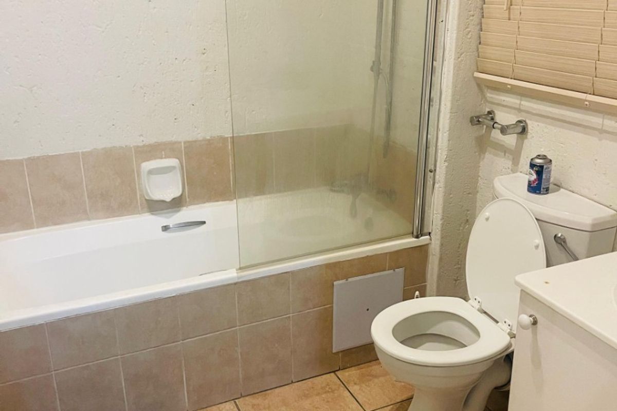 A functional bathroom featuring a tiled bathtub with a glass shower screen, a standard toilet, and tiled flooring.