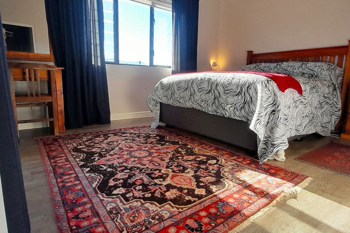 A well-lit bedroom featuring laminate flooring, large windows with dark curtains, and neutral wall finishes.