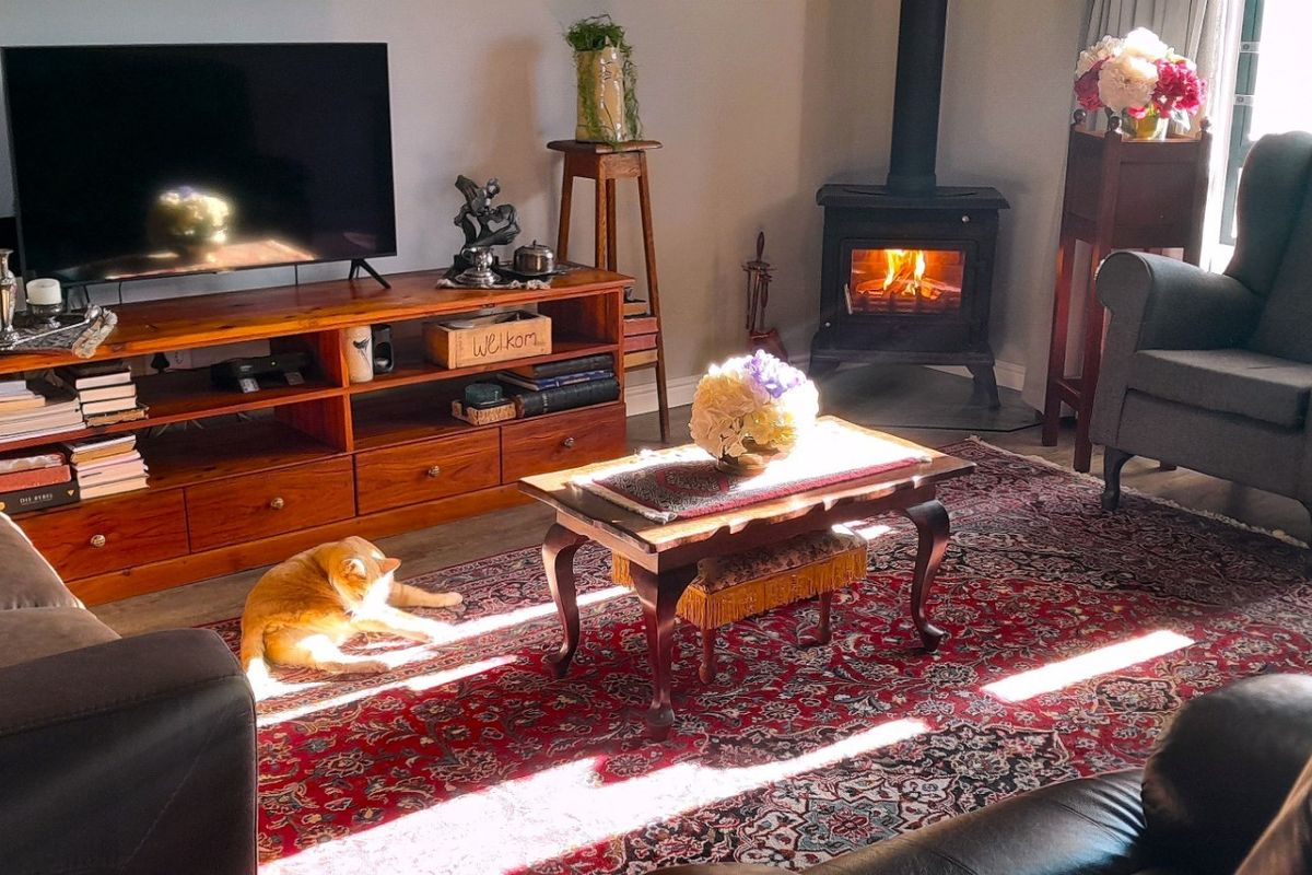 A cozy living room featuring a cast iron wood-burning fireplace, tiled flooring, and large windows allowing for natural light.