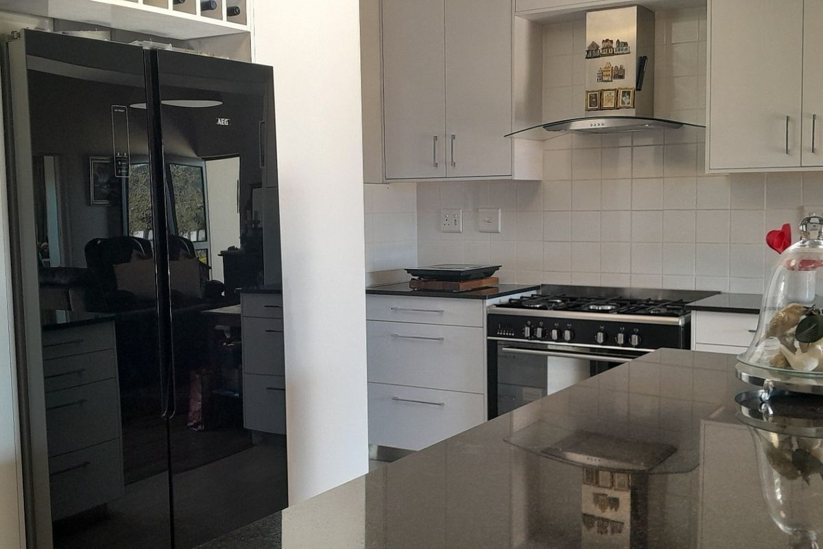 Modern kitchen featuring sleek white cabinetry, dark stone countertops, a gas hob with stainless steel extractor fan, and a large integrated-style refrigerator.