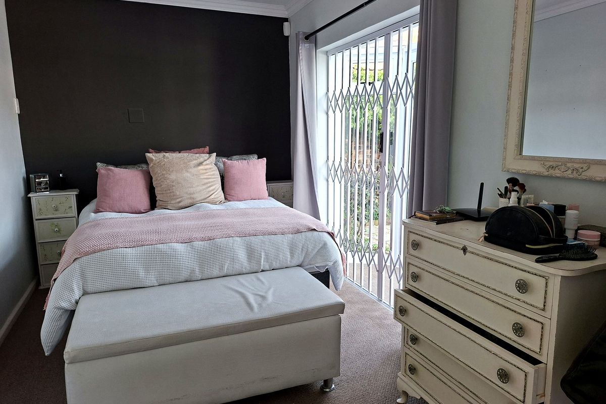A well-maintained bedroom featuring a dark accent wall, carpeted flooring, and a sliding glass door with a security gate leading to the exterior.