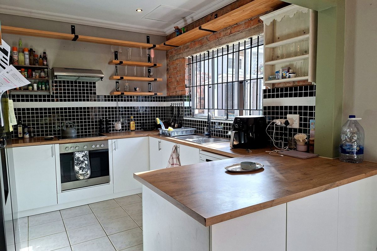 A functional kitchen featuring white cabinetry, wooden countertops, black tiled splashbacks, and an exposed brick feature wall with open shelving.