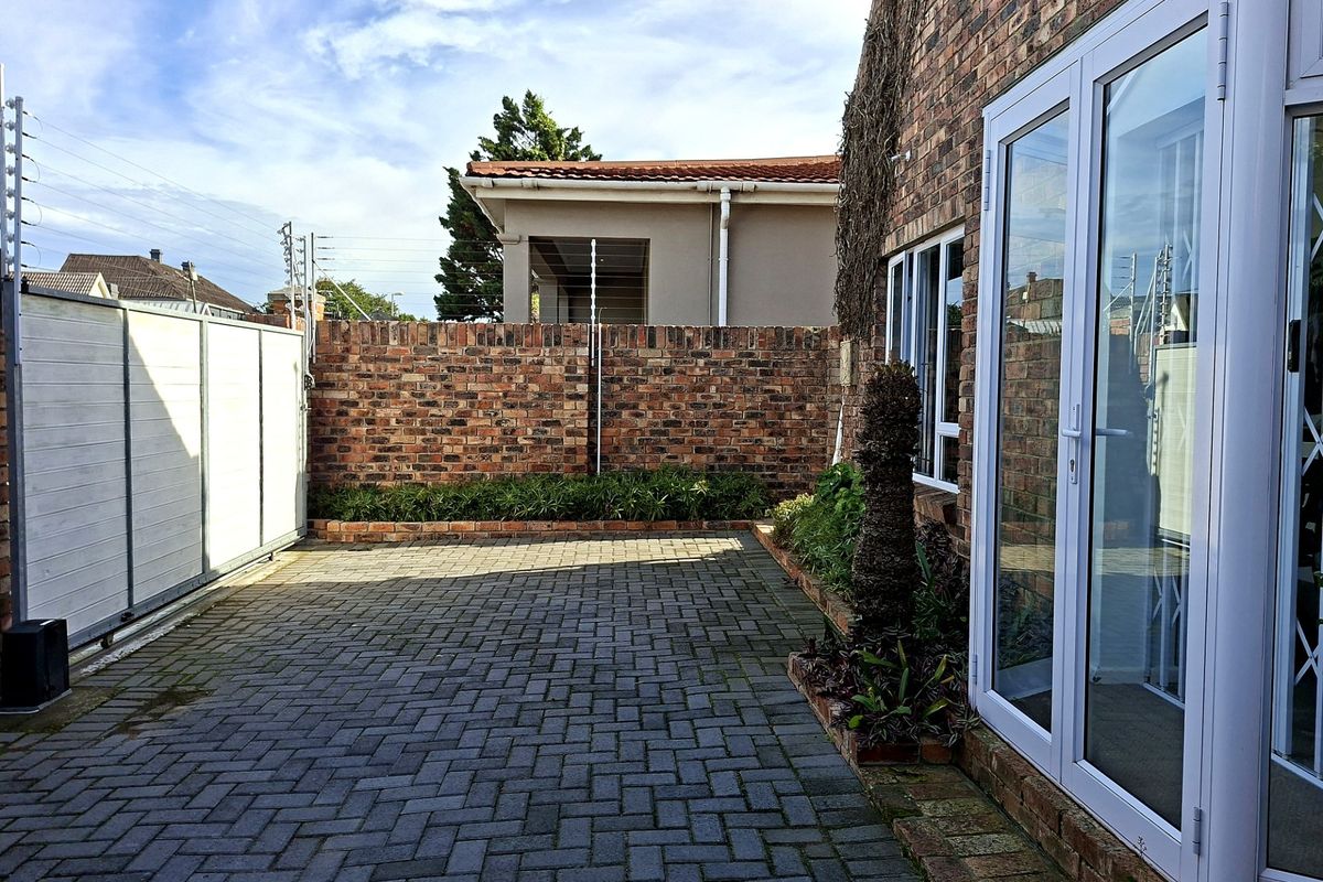 A private rear courtyard featuring brick paving, a secure facebrick boundary wall with electric fencing, and white aluminium glass doors leading into the home.