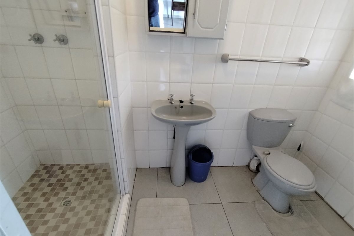 A functional bathroom featuring a glass-enclosed shower, pedestal basin, and toilet with white wall tiling and neutral floor tiles.