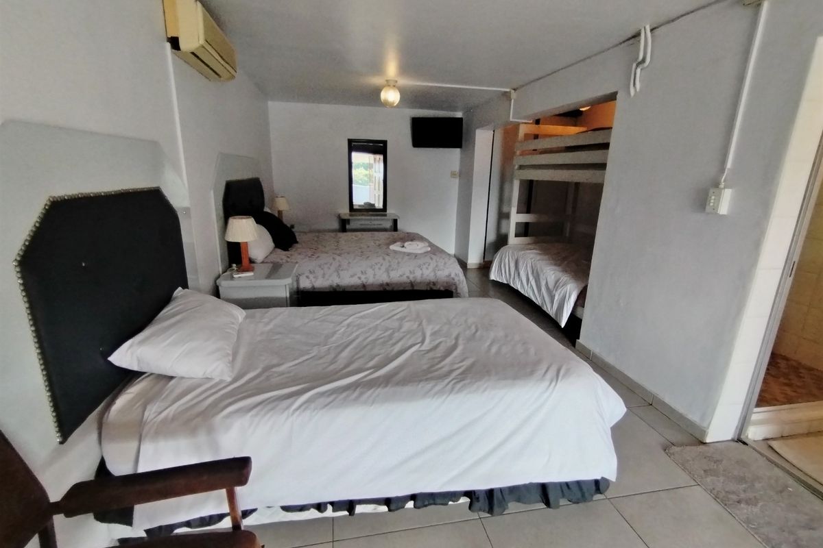 A spacious bedroom featuring multiple sleeping areas, including a bunk bed configuration, tiled flooring, and wall-mounted air conditioning unit.