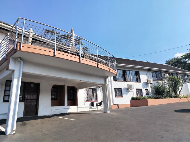 Exterior view of the lodge featuring a large elevated balcony with stainless steel railings, asphalt driveway, and white facade with casement windows.